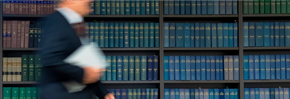 Symbolbild: Mann l&auml;uft vor einem B&uuml;cherregal durch